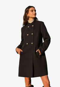 Cappotto di lana nera con taglio dritto, design doppiopetto, bottoni dorati e tasche laterali. Collo a costine e maniche lunghe.