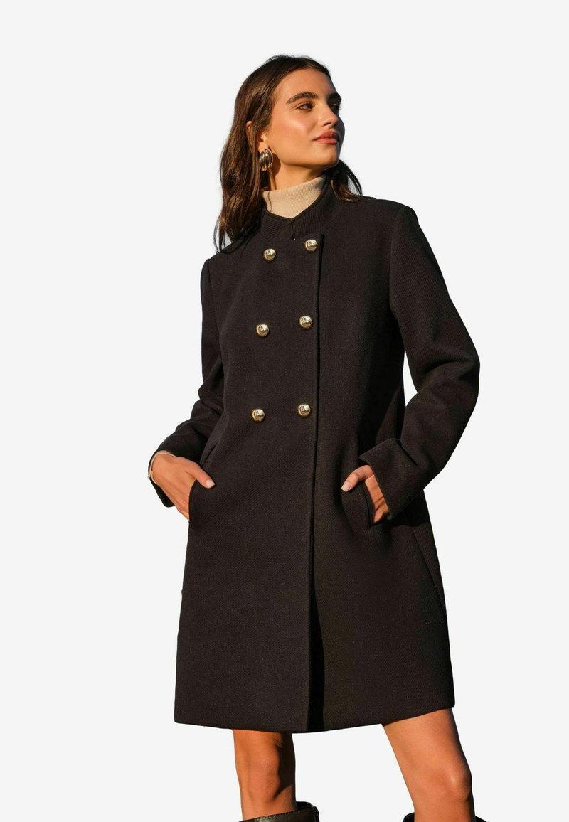 Cappotto di lana nera con taglio dritto, design doppiopetto, bottoni dorati e tasche laterali. Collo a costine e maniche lunghe.