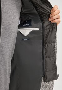 Graue Jacke mit glattem Innenfutter. Verfügt über Innentaschen mit den Aufschriften "JOOP!" und "SLIM FIT." Reißverschlussverschluss und gesteppte Textur sichtbar.