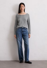 Szara góra z długim rękawem w połączeniu z wyblakłymi niebieskimi spodniami typu straight-leg. Stylizacja ma swobodny krój i prosty design. Czarne buty dopełniają całość.