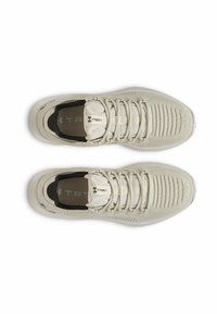 Lyse beige sportsko med tekstureret overdel, kontrastfyldt sort inderside, flade snørebånd og polstret tunge. Har ribbet design på tåområdet.