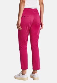Pantalons roses ajustés avec deux poches arrière, texture lisse et design à jambes effilées. Portés avec des baskets blanches, détail de taille visible.