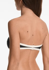 Črn bandeau bikini zgornji del z belimi poudarki, z gladko teksturo in zaponko na hrbtni strani za zapiranje. Prikazan zadnji pogled.