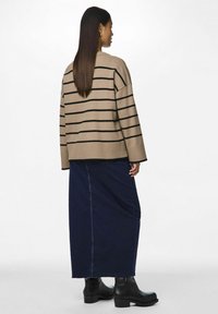 Pull en beige rayé, coupe ample, avec des poignets côtelés. Associé à une longue jupe en denim foncé et des bottines noires. Look simple et décontracté.
