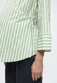 Πουκάμισο με πράσινες και λευκές ρίγες, με σχέδιο τύπου wrap, δεμένο στο πλάι, με καμπυλωτό τελείωμα και μακριά μανίκια με ριγέ μανσέτες.
