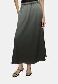 Lunga gonna grigia scura fluente realizzata in tessuto leggero, con vita elastica e tasche laterali, abbinata a sandali neri con tacco.