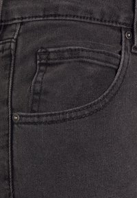 Jeans em denim preto com um bolso frontal com borda costurada e rebite de metal, apresentando uma superfície de tecido suave e texturizada.