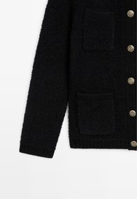 Manica di cardigan nera con texture, due tasche frontali a toppa e bottoni decorativi dorati sulla patta anteriore.