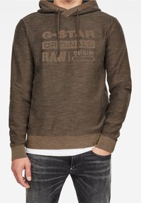 Hnědá mikina s kapucí s texturovaným povrchem, s kapucí na stahovací šňůrce a vyraženým logem "G-Star RAW" na přední straně. Žebrované manžety a spodní lem.
