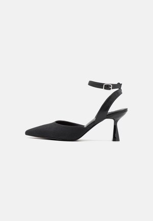 Black slingback heels made of textured material with a pointed toe and a glossy black heel. An adjustable ankle strap features a metallic buckle.