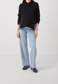 Black hooded sweatshirt, loose fit, paired with light blue wide-leg jeans. The jeans have a frayed hem, complemented by dark blue athletic shoes.