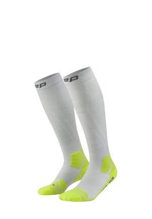 White knee-high compression socks with neon yellow heel, toe, and sole accents, designed for performance and support.