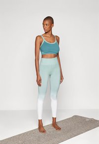 Turkooizen sportbeha en legging met verloop van lichtblauw naar wit, met een zachte textuur. Inclusief yogamat eronder.