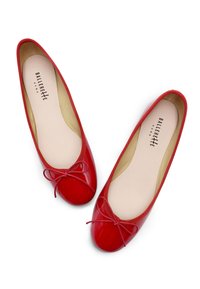 Ballerines en cuir verni rouge avec un bout arrondi, ornées d'un fin nœud et d'un bord élastique texturé autour de l'ouverture. L'intérieur est beige.