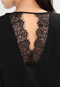 Vêtement noir avec un dos en V profond orné de détails en dentelle noire complexe, mettant en valeur la texture et la transparence.