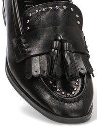 Mocasín de cuero negro con borlas, flecos decorativos y tachuelas plateadas en el borde. Textura suave y diseño de puntera puntiaguda.