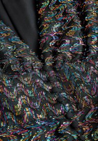 Zwarte stof met golvende, meerkleurige stikpatronen. Heeft ronde zwarte knopen en textuurrijke accenten in levendige tinten.