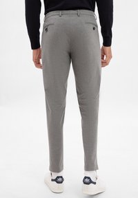 Gray tailored trousers with a subtle texture, two back pockets, and a slim fit, paired with white sneakers and light-colored socks.