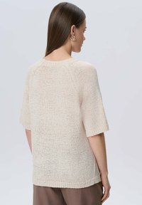 Jasno beżowy sweter dzianinowy z krótkimi rękawami, okrągłym dekoltem i fakturowanym wzorem. Posiada luźny krój i prążkowany dół.