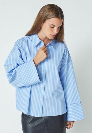 Light blue button-up shirt with white vertical stripes and wide sleeves, featuring a pointed collar and smooth fabric texture.
