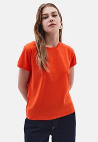 Krátký rukáv oranžové bavlněné tričko s kulatým výstřihem a jednoduchým designem, nošené s tmavě modrými džíny.