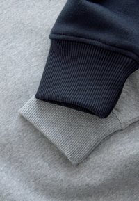 Manșetele unui hanorac gri și bleumarin cu textură în relief. Manșeta gri are un finisaj mai deschis și moale, în timp ce manșeta bleumarin este mai groasă și mai închisă la culoare.