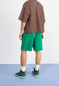 Brown short-sleeve shirt, green shorts, and dark sneakers with light accents. Relaxed fit, cotton material, rear view displayed.