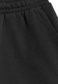 Gros plan sur la ceinture élastique noire et la poche latérale sur un pantalon ou un short en tissu tricoté doux.