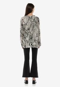 Koszulka z długim rękawem w czarno-białe paski zebry, z luźnym krojem, zaokrąglonym dołem i fakturowanym materiałem, w połączeniu z czarnymi spodniami dzwonami.