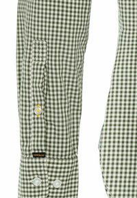 Tela de camisa de cuadros verde y blanca con puños abotonados; presenta una textura sutil y una etiqueta en la manga izquierda.