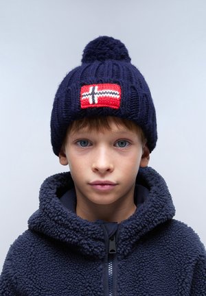 Marinblå stickad mössa med en pom-pom och en röd lapp med ett vitt kors. Bärs med en marinblå fleecejacka med hög krage.