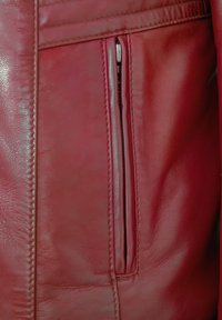 Rote Lederjacke mit glatter Textur, die eine mit Reißverschluss versehene Tasche auf der linken Seite hat. Sichtbare Nähte verleihen dem Design Detail.