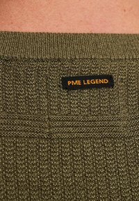 Olivovozelený pletený sveter s textúrovaným vzorom. Má rebrovaný golier a čiernu nálepku s nápisom "PME LEGEND" v oranžovej farbe.