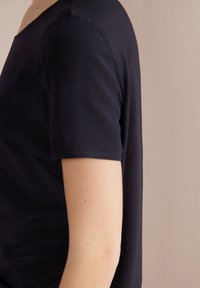 Top blu navy a maniche corte con scollatura ampia. Tessuto morbido e liscio che si adagia vicino al corpo. Linee pulite e design minimal.