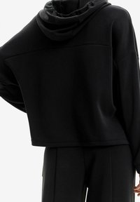 Sudadera corta negra con capucha ajustable y corte relajado. Textura suave y detalles de costura mínimos, combinada con pantalones a juego.