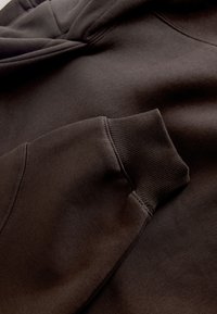 Közeli kép egy sötétbarna pulóver ujjáról, amely bemutatja a bordázott mandzsetta varrását és a szövet textúráját.