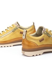 Zapatos de cuero amarillos con un tacón de acento marrón, que cuentan con una cremallera lateral, una suela texturizada y un forro interior a cuadros. Detalles de costura contrastante.
