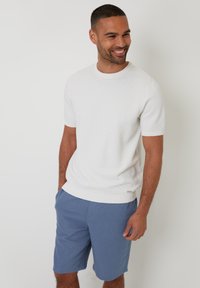 Bílý strukturovaný svetr s krátkým rukávem a kulatým výstřihem, ve spojení se světle modrými šortkami. Tento outfit má jednoduché, čisté linie.