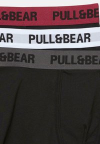 Három pár fekete alsónadrág, eltérő színű, bordó, szürke és fehér elasztikus derekakkal, mindegyiken vastag, fekete betűkkel a "PULL&BEAR" felirat található.