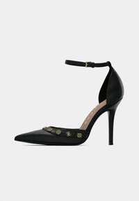 Crna kožna salonka s visokom petom, šiljastim vrhom, remenčićem oko gležnja i zlatnim ukrasnim detaljima. Glatka tekstura i dizajn štikle.