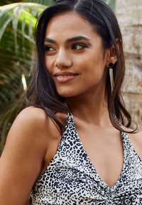 Leopard print halter top featuring a twist front design, made of lightweight fabric. Includes drop earrings with silver strands and circular accents.