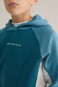 Tyrkysová mikina s kapucí a bílým logem "BLUE RIDGE DENIM" na hrudi. Nabízí pohodlný střih a texturovanou látku s kontrastními světle modrými akcenty.