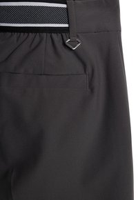 Primo piano di una tasca di pantaloni grigio scuro con una cintura elastica a righe black and white e un piccolo anello metallico triangolare attaccato.