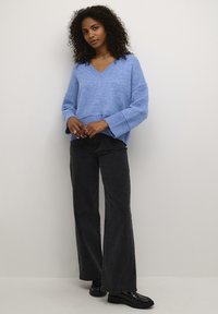 Lichtblauwe gebreide trui met een V-hals en drop sleeves, gecombineerd met hoge zwarte flared jeans en zwarte plateau schoenen.