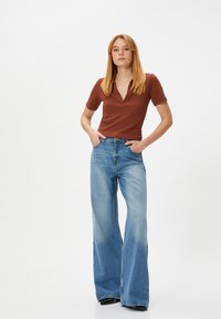 Bruine polo met korte mouwen en V-hals, gecombineerd met vervaagde blauwe wijde jeans, voorzien van een klassiek vijf-pocket ontwerp en lichte slijtage.