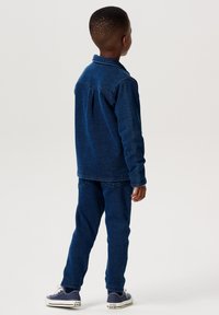 Jeansjacka och byxor i mörkblått. Jackan har krage och långa ärmar; byxorna har en rak passform. Ett par avslappnade skor fulländar looken.