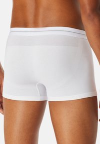 Hvide boxershorts med en glat tekstur, der har en kontrastfarvet meshbind ved taljen og en tætsiddende pasform omkring benene.
