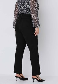 Schwarze Jeans im geraden Schnitt, hohe Taille und Gesäßtaschen. Getragen mit einer grauen, durchsichtigen Bluse mit Leopardenmuster und schwarzen Slingback-Heels.