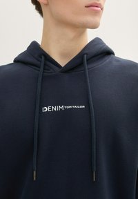 Námornícka mikina s kapucňou vyrobená z bavlneného zmesi. Na prednej strane je biely logo "DENIM TOM TAILOR", šnúrky s kovovými koncami.