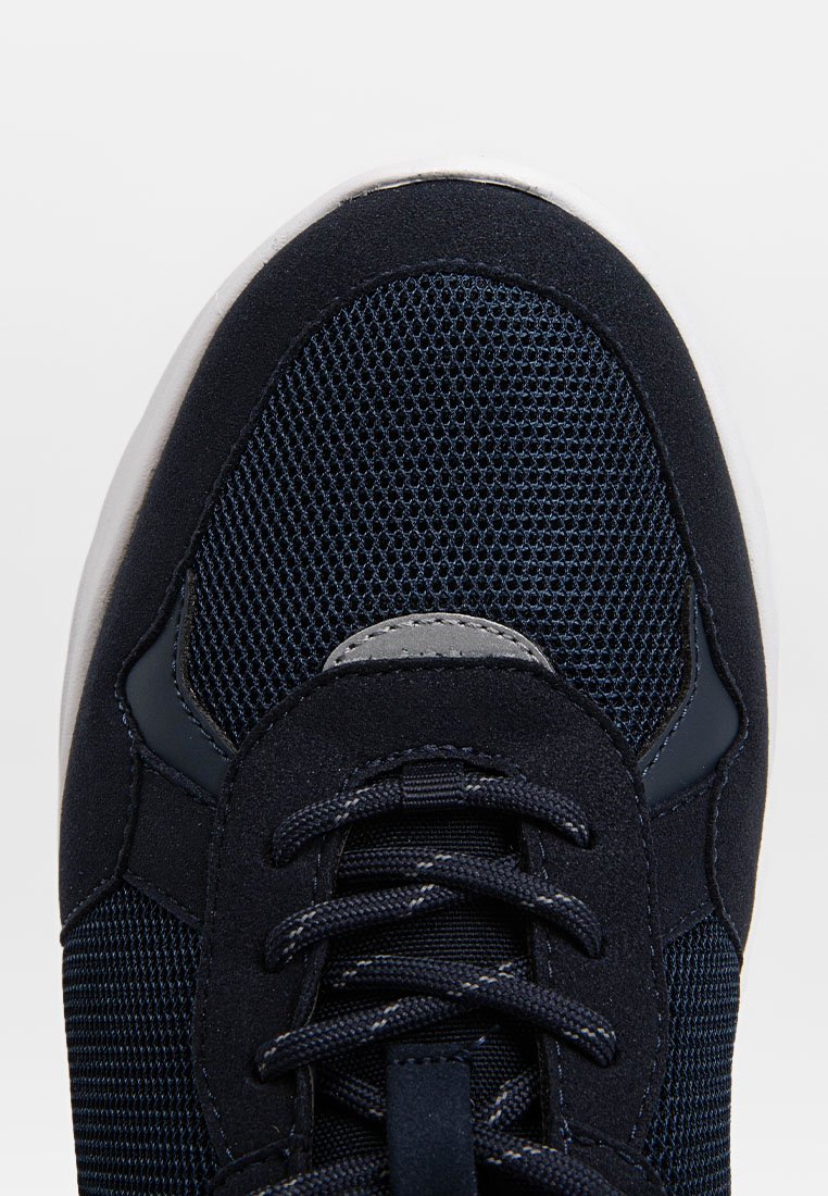 Baskets bleu marine avec tige en mesh, accents en daim et lacets à plat. Présente un design latéral incurvé et une semelle blanche contrastante.